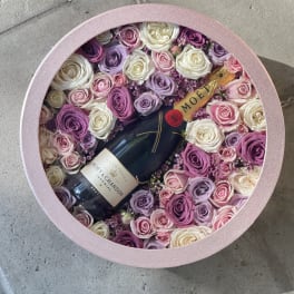 Round pink box filled with roses and a champagne bottle