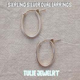 Pair of silver oval hoop earrings on a textured fabric background