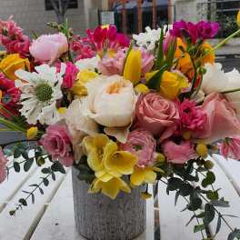 Colorful arrangement of pink roses, yellow blooms, and mixed flowers in a gray textured vase