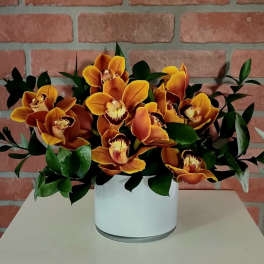Orange orchids arranged in a white vase