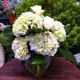 White hydrangeas and roses arranged in a metallic vase