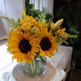 Sunflowers and yellow roses arranged in a clear glass vase