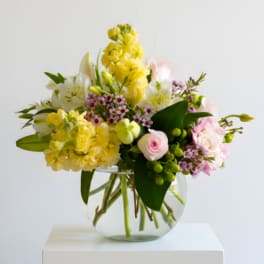 Mixed bouquet of yellow, pink, and white flowers in a clear glass vase.