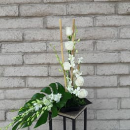 Tall white floral arrangement with roses and orchids in a black container