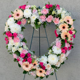 Heart-shaped floral wreath with pink, white, and peach flowers on a stand