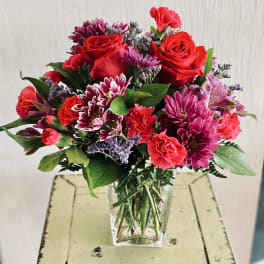 Bouquet of red roses, pink carnations, and purple chrysanthemums in a clear vase