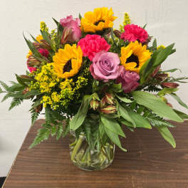 Mixed bouquet of sunflowers, roses, and carnations in a glass vase