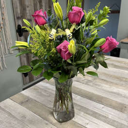 Pink roses and yellow lilies in a clear glass vase with bee decorations