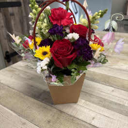 Mixed bouquet with red roses, yellow daisies, and purple flowers in a handled box