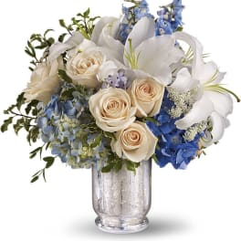 White lilies, cream roses, and blue hydrangeas in a glass vase