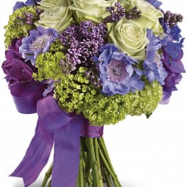 Bouquet of white roses, purple flowers, and green hydrangeas tied with a purple ribbon