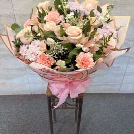 Large bouquet of pink and peach flowers wrapped in pink paper with a ribbon