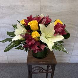Bouquet of yellow roses and white lilies with burgundy flowers in a dark vase