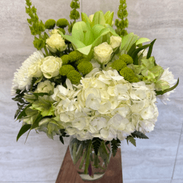 Tall white and green flower arrangement with hydrangeas and roses in a clear glass vase