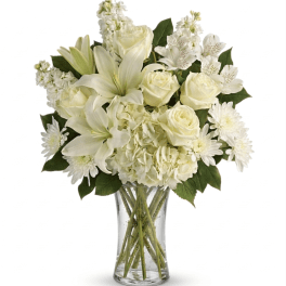 All-white bouquet of lilies, roses, hydrangeas, and other blooms arranged in a clear glass vase