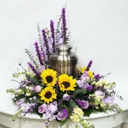 Purple and yellow floral arrangement around a silver urn