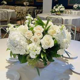 White rose and hydrangea centerpiece in a low bowl on a round table