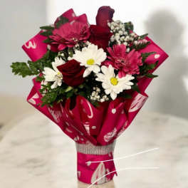 Bouquet of red roses, pink gerbera daisies, and white daisies wrapped in bright pink paper