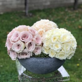 Three rose bouquets in pale pink, cream, and white arranged in a dark bowl