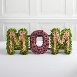 Floral arrangement spelling MOM with pink flowers and green foliage