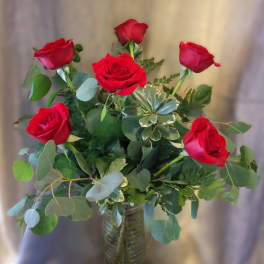 Red roses arranged in a clear glass vase with mixed greenery