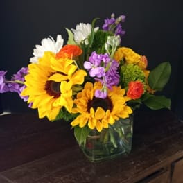 Mixed bouquet with sunflowers, daisies, and purple flowers in a glass vase