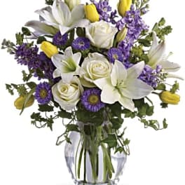 Mixed bouquet of white lilies and roses with purple and yellow flowers in a clear glass vase