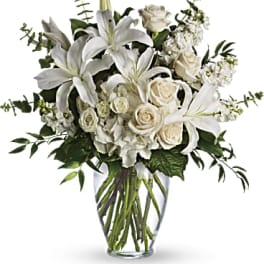 Tall arrangement of white lilies, roses, and hydrangeas in a clear glass vase