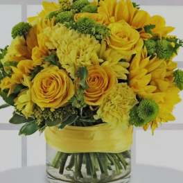 Yellow roses and sunflowers arranged in a glass vase with a yellow ribbon.