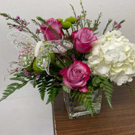 Pink roses and white hydrangea in a glass vase with a decorative butterfly