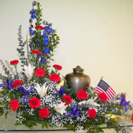 Red carnations and blue flowers arranged with white lilies and an American flag