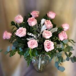 Pink roses arranged in a clear glass vase with mixed greenery.