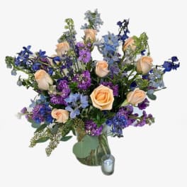 Peach roses and blue-purple flowers in a glass vase with a candle