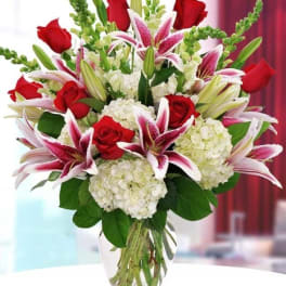 Bouquet of red roses, pink lilies, and white hydrangeas in a glass vase