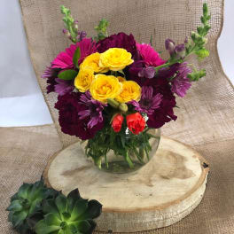 Mixed bouquet of yellow, pink, and purple flowers in a clear glass vase