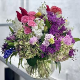 Mixed bouquet of pink, purple, white, and blue flowers in a clear glass vase