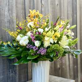 Mixed bouquet in a tall white vase with yellow, white, pink, and purple flowers.