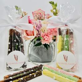 Flower arrangement with pink and peach roses beside wrapped chocolate-covered pretzels