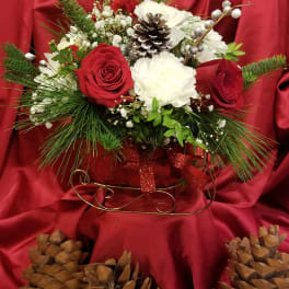 Red and white floral arrangement with pinecones and ribbon in a decorative holder