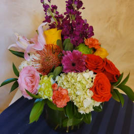 Mixed bouquet in a dark vase with roses, lilies, hydrangea, and bright accent flowers