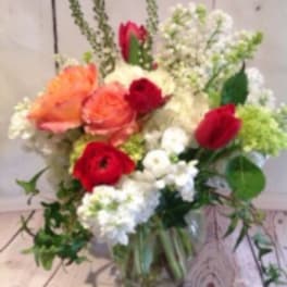 Mixed arrangement of peach roses, red blooms, and white flowers in a clear glass vase