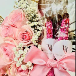 Pink roses with baby's breath and pink gift items tied with a satin bow