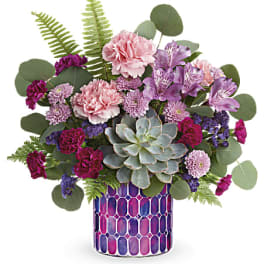 Mixed pink and purple flowers in a patterned vase with a succulent centerpiece