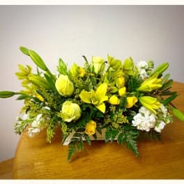 Yellow lilies and roses arranged with white flowers in a low centerpiece