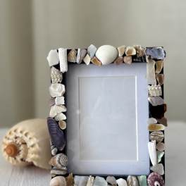 Shell-covered photo frame on a table with a seashell ornament behind it