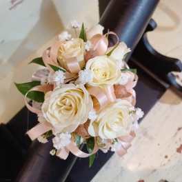 Small ivory rose corsage with peach ribbon and tiny white filler flowers in a round design