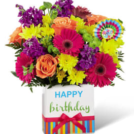 Bright mixed bouquet in a birthday gift box with a colorful rosette.