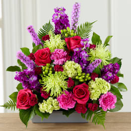 Bright mixed bouquet with roses, carnations, and purple blooms in a rectangular vase