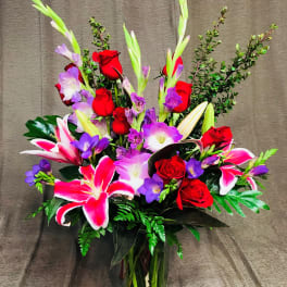 Bouquet of red roses, pink lilies, and purple flowers in a glass vase