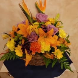 Basket arrangement of orange lilies, purple roses, and yellow daisies
